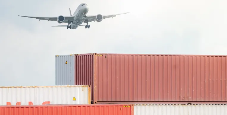 TOP Worldwide cargo containers stacked at a port with a plane flying overhead, symbolizing integrated global freight solutions by air, sea, and land for complex shipping challenges.